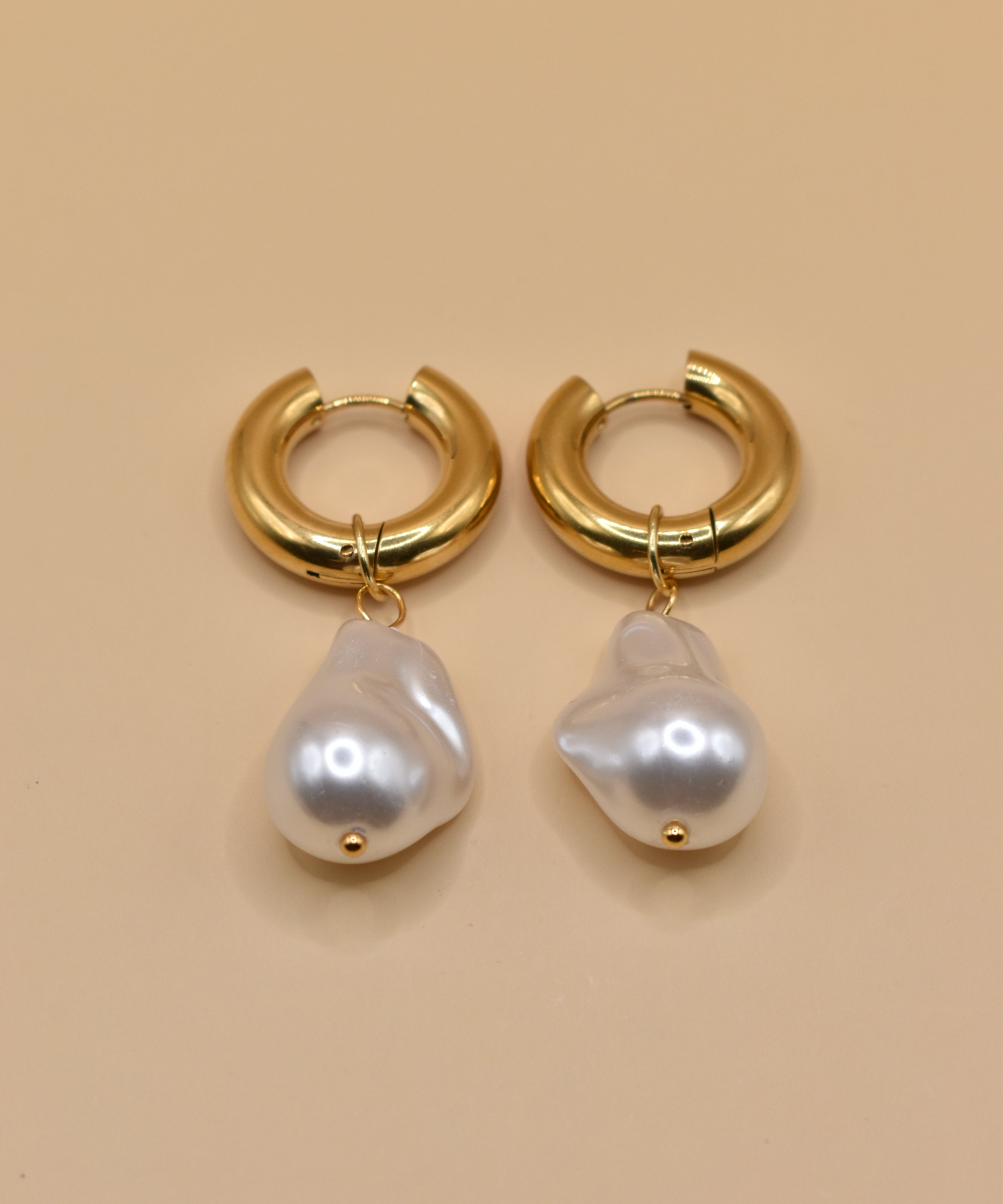 Gold huggies earrings with pearl drop on white background