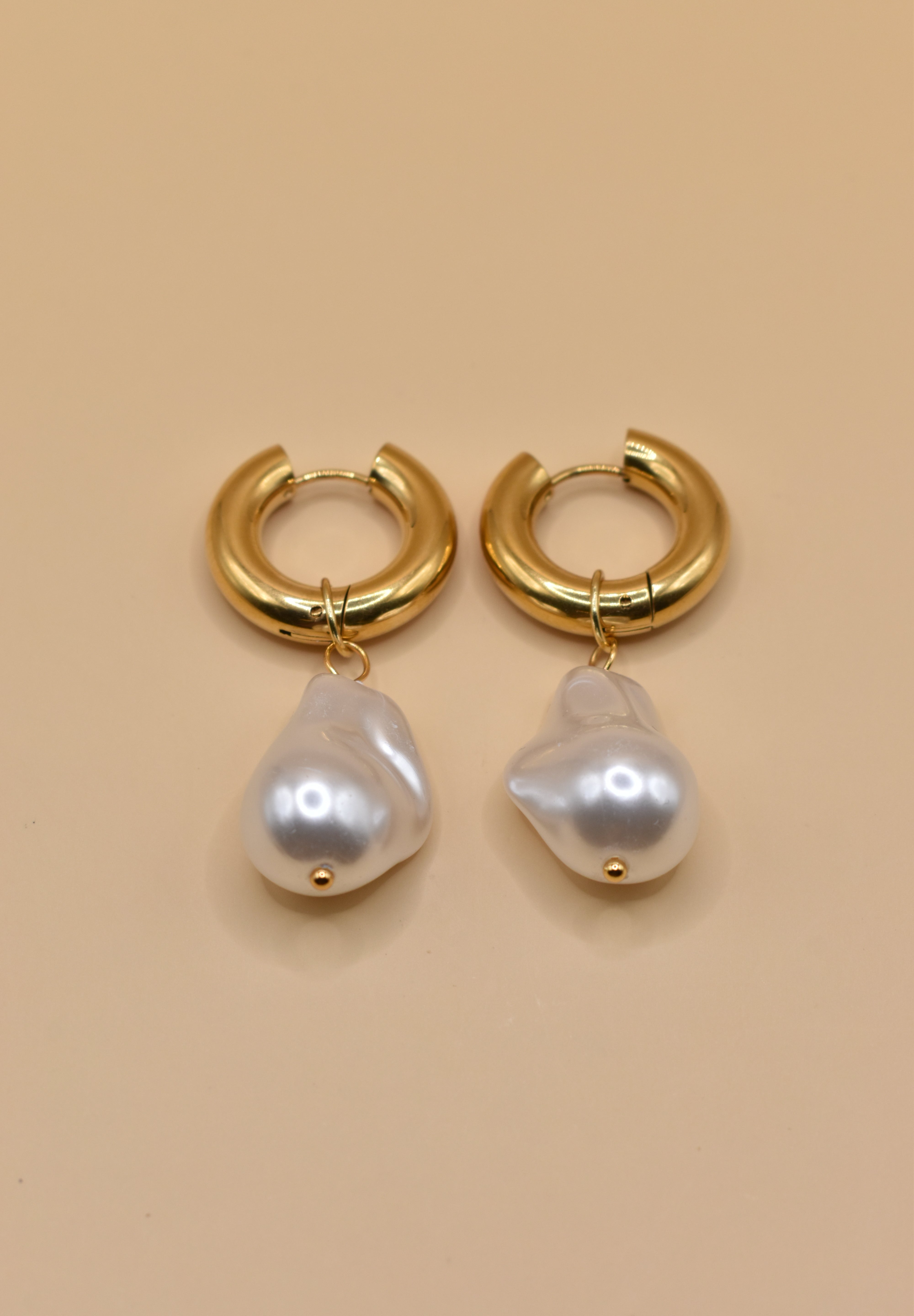 Gold huggies earrings with pearl drop on white background