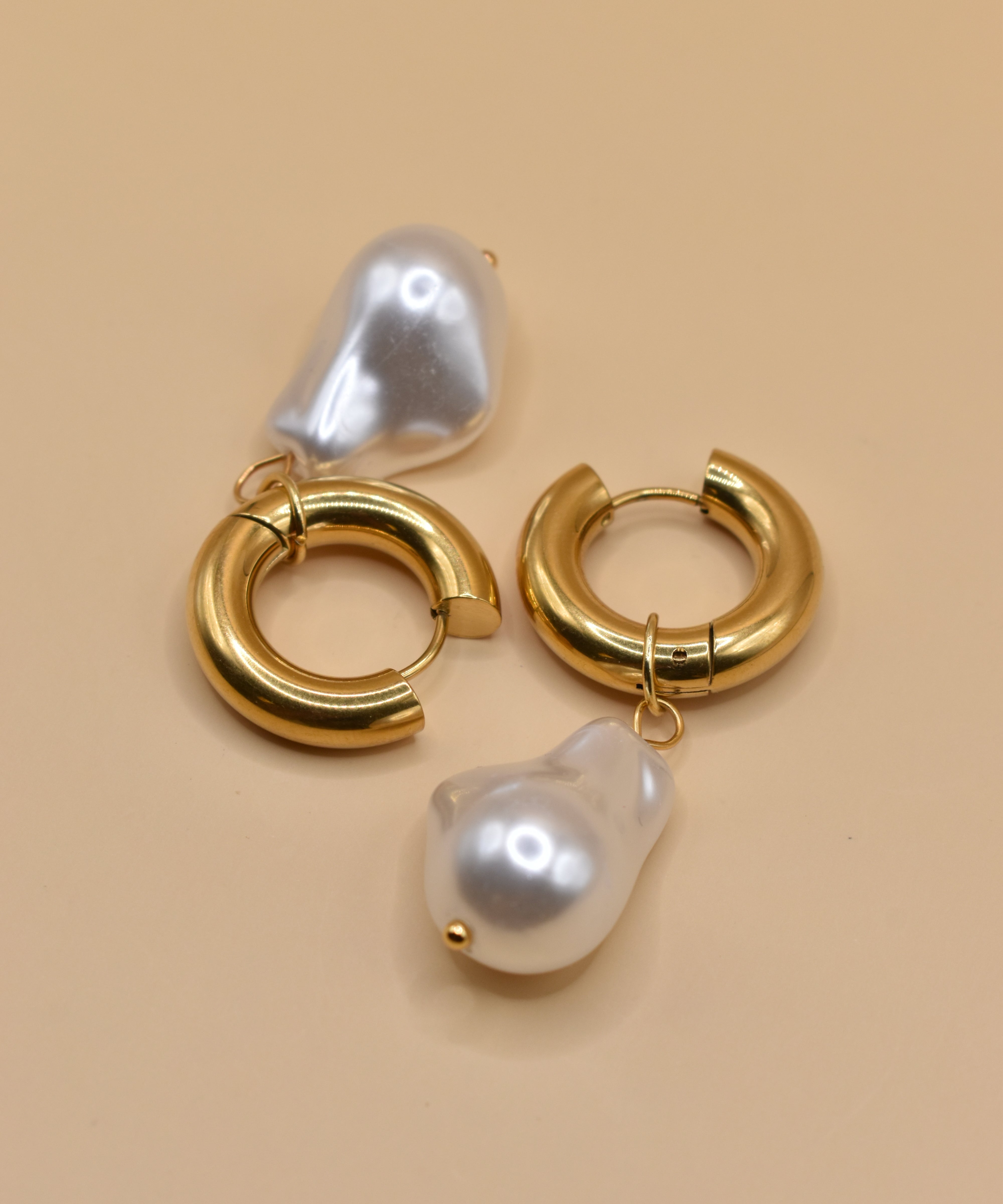 Gold huggies earrings with pearl drop on white background