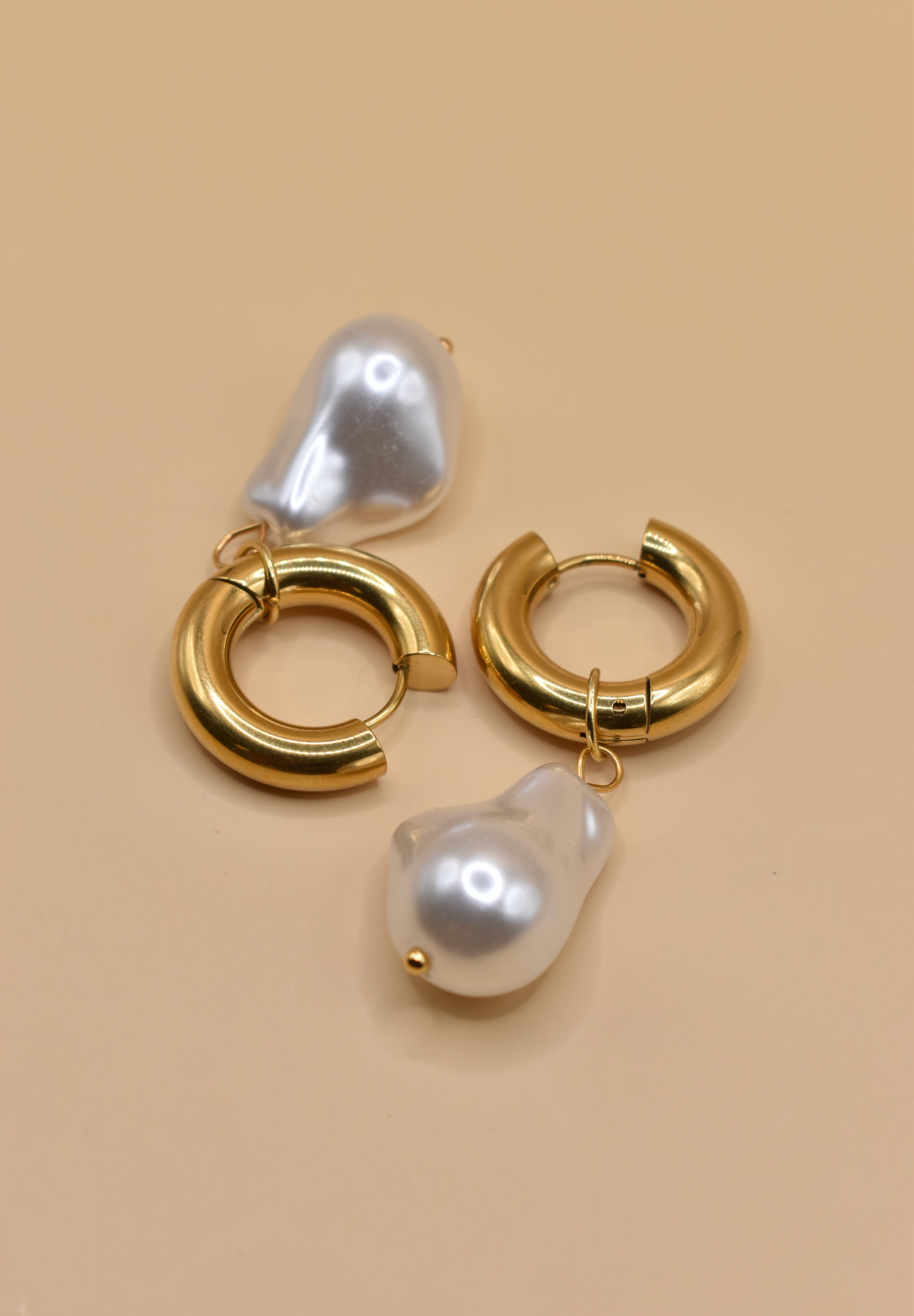 Gold huggies earrings with pearl drop on white background