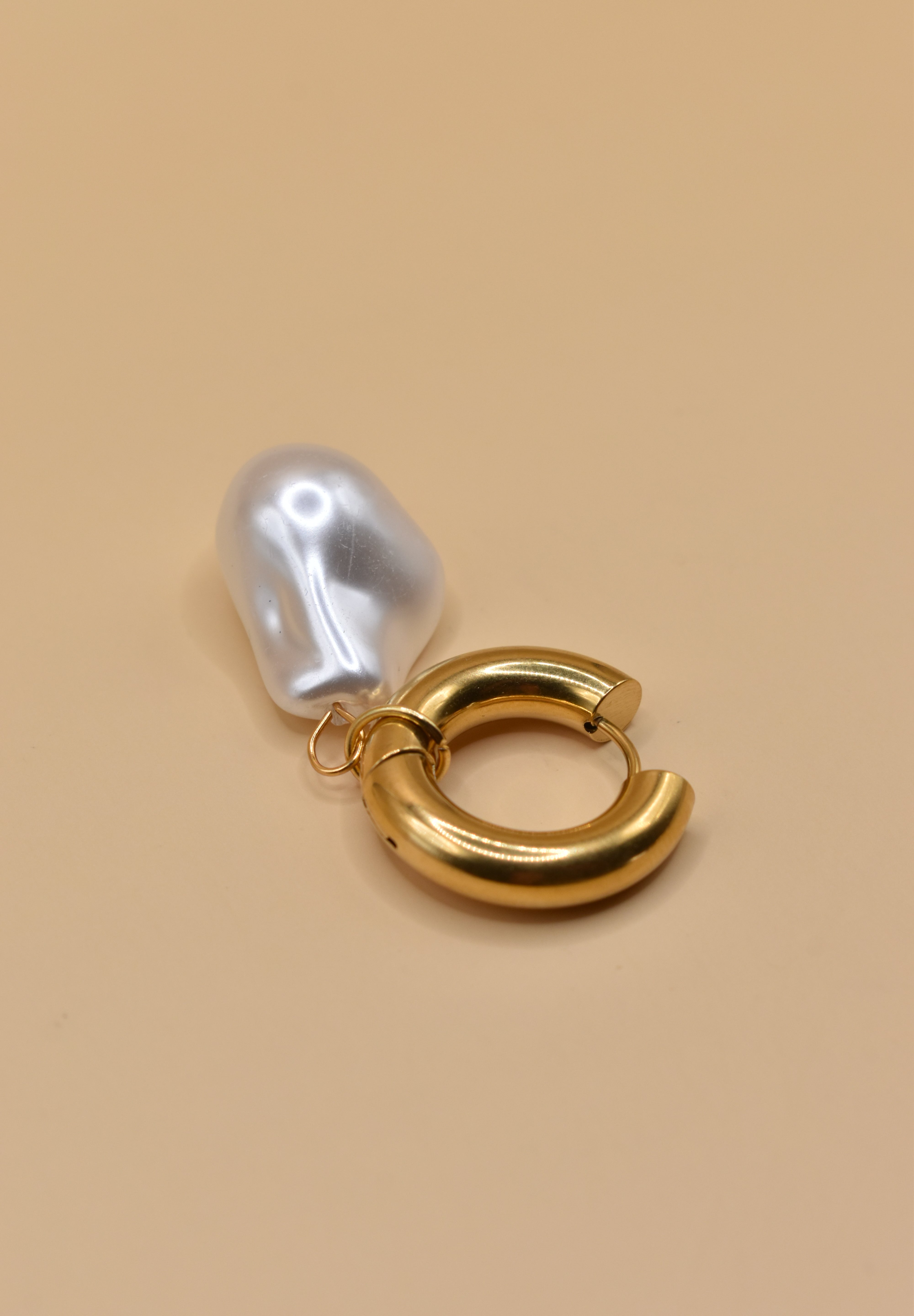Gold huggies earrings with pearl drop on white background